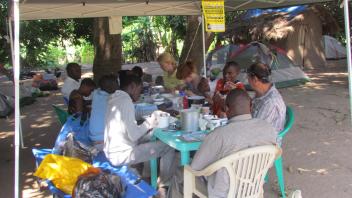 Many people sit at a table sorting mosquito specimines