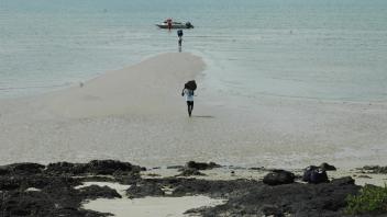 A boat in the water behind a sandy peninsula. People carry bags from the boat to the shore.