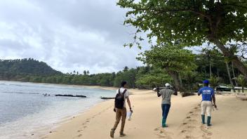 Three people walking along a sandy beach by a calm bay under a cloudy sky