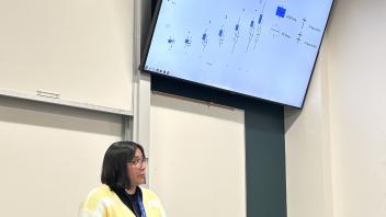 An undergraduate presents a powerpoint presentation from the front of a classroom.