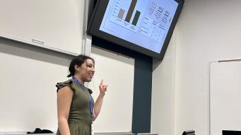 An undergraduate presents a powerpoint presentation from the front of a classroom.