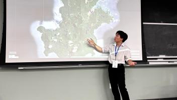 An undergraduate presents a powerpoint presentation from the front of a classroom.