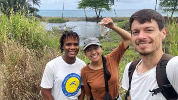 Three smiling hikers by a tropical lagoon with palm trees and tall grass