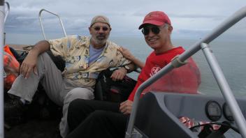 Two people in ball caps on a boat smiling at the camera