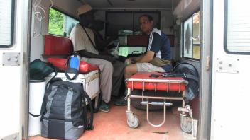Two people sit inside the back of a small ambulance filled with backpacks