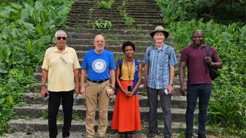 Five people pose for the camera in front of stairs surrounded by lush green foliage