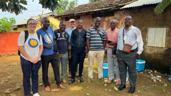 Eight people pose casually for a photo outside a home.