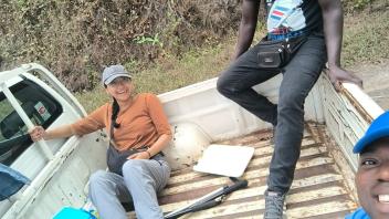 Three men smiling in a pickup truck bed with a blue cooler and dirt hillside