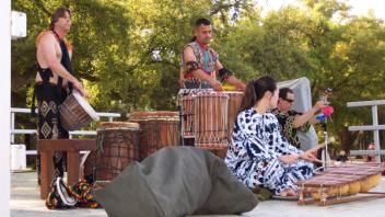 A band plays traditional drums and xylophone outdoors in traditional dress