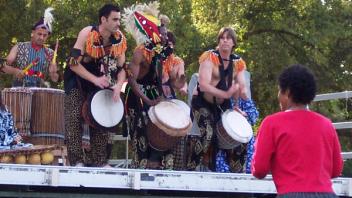 A band plays traditional drums outdoors in traditional dress