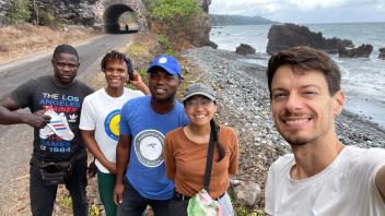 Five smiling people on a rocky coastal trail with ocean and cliff tunnel