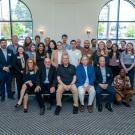 Indoor group portrait: ~36 diverse adults seated and standing before arched windows