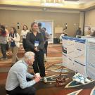 Claire stands in front of her poster while an older gentleman crouches to read it better