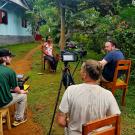 A person is filmed and interviewed by three others all seated in chairs outside.